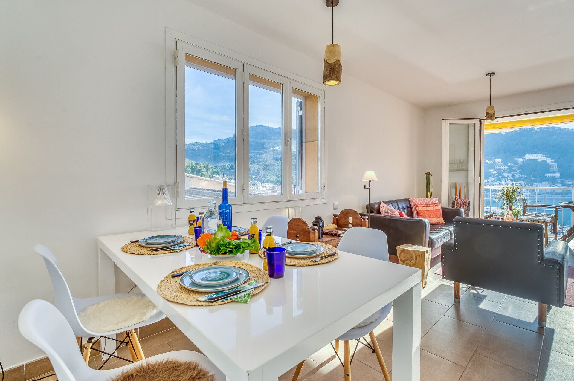 Een eetgedeelte met een witte tafel gedekt voor twee personen, uitzicht op zee en een balkon met bergzicht.