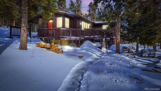Eine Hütte mit einer Terrasse, umgeben von Schnee und Bäumen.