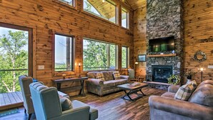 A spacious living room with a stone fireplace, large windows, and wooden walls. - Mtn Views, Fireplace, & 2-Story Wall of Windows!🔥 (Sevierville)