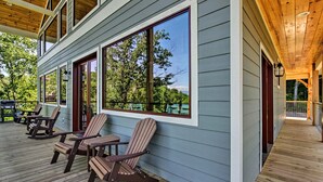 A covered deck with Adirondack chairs and a grill, overlooking a wooded area. - Mtn Views, Fireplace, & 2-Story Wall of Windows!🔥 (Sevierville)
