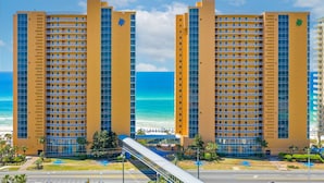 A high-rise hotel with multiple balconies, a beach view, and a pedestrian bridge.