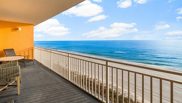 A balcony with a view of the ocean, a table, and chairs.