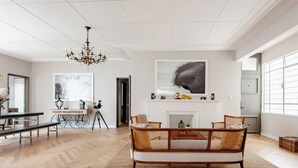 Ett rymligt vardagsrum med ett fiskbensmönstrat golv, en kristallkrona, en öppen spis och en stor, abstrakt målning.