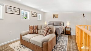 A modern bedroom with a bed, a sofa, a wooden railing, and a small table. - Quiet and Cozy getaway cabin in Hatcher Pass, Alaska; 15 min. from Palmer! (Palmer)