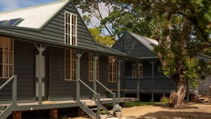 A row of dark wooden buildings with multiple windows and a covered porch area. - 20 People / 9 Bedroom / 13 Beds Cabin Compound in the heart of Huskisson (Huskisson)
