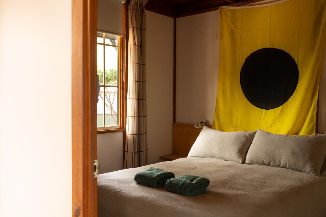 A room with a bed, a yellow curtain with a black circle, and a window with bamboo blinds.