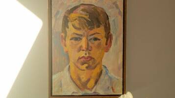 A framed portrait on a wall with a vase of white flowers to the right.