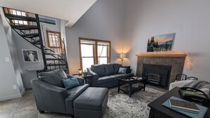 A modern living room with a fireplace, a sofa set, a coffee table, and a staircase. - Nature's Nook | In-Town | Pool | Hot Tub (Durango)