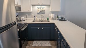 A compact kitchen with white cabinets, a stainless steel refrigerator, a microwave, a sink, and a decorative sign above the sink. - Nature's Nook | In-Town | Pool | Hot Tub (Durango)