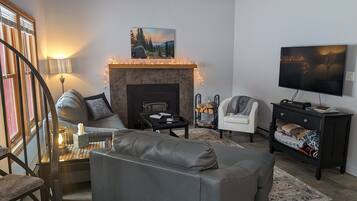 Ein Wohnzimmer mit Kamin, Sofa, Sessel und Fernseher.