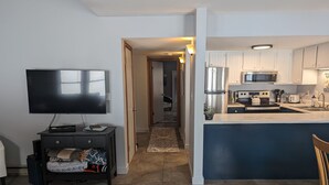 A modern living room with a flat-screen TV, a sofa, and a dining area with a kitchen in the background. - Nature's Nook | In-Town | Pool | Hot Tub (Durango)