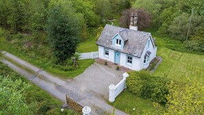 A white house with a grey roof, surrounded by lush greenery and a gravel driveway. - 1 bedroom accommodation in Carlisle (Carlisle)