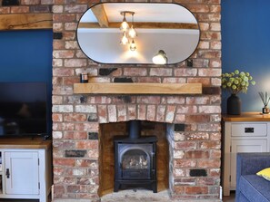 A brick fireplace with a wooden mantel, a mirror above it, and a TV on the left. - 3 bedroom accommodation in Slingsby, near Malton (Slingsby, near Malton)