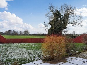 Un paysage rural avec un grand arbre, une clôture rouge et un champ herbeux parsemé de plaques de neige.