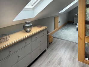 Une chambre moderne avec une lucarne, des meubles de rangement gris, une commode en bois et un tapis gris.