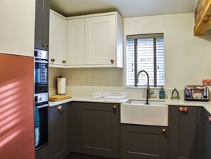 A kitchen with a built-in oven, a sink, and a window with blinds.