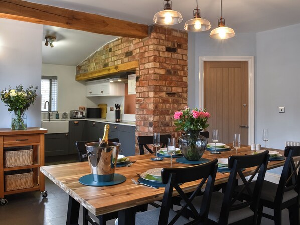 A dining area with a wooden table set for four, a brick column, and pendant lighting.