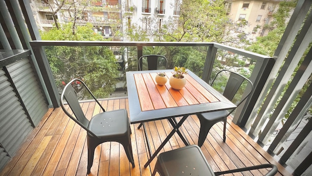 A balcony with a wooden table and chairs, two potted plants, and a view of buildings and trees. - Apartments Bariloche - Palermo Viejo, Cerviño (Buenos Aires)