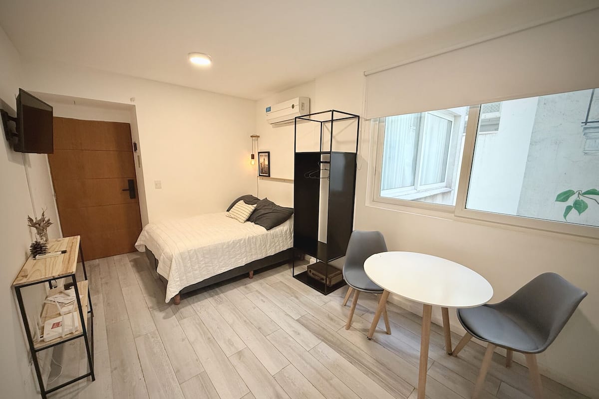Ein kleiner, moderner Raum mit einem Bett, einem Tisch, zwei Stühlen, einem Fernseher und einem Fenster.