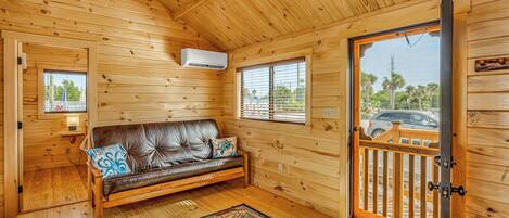 Ein gemütliches Blockhäuschen-Interieur mit Holzausstattung, einer Ledersofa, einem Teppich und Blick durch eine Tür.