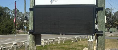 Une enseigne du « Good Times Motel & Marina » avec un panneau d’affichage numérique, entourée d’une barrière en corde et d’une couche de paillis au sol.