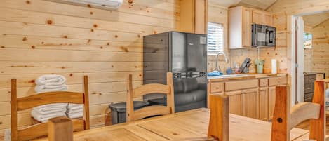 Interior de una cabaña de madera con comedor, cocina y vistas al exterior.