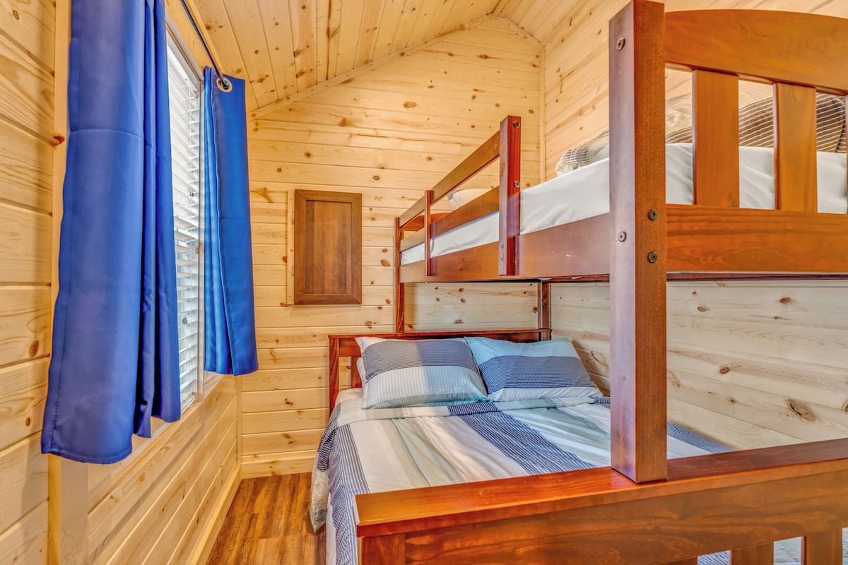 A wooden cabin room with bunk beds, a window with curtains, and a wooden door.