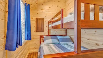 A wooden cabin room with bunk beds, a window with curtains, and a wooden door.