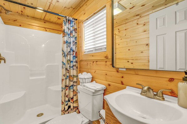 A wooden-paneled bathroom with a white bathtub, a sink with a gold faucet, and a toilet with a basket of towels.