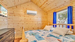 A wooden cabin room with a bed, a dresser, a TV, and a window with curtains. - Good Times Motel and Marina  (Steinhatchee)