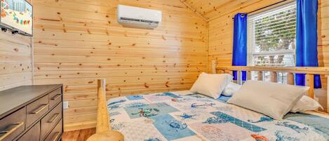 Habitación de cabaña de madera con cama, cómoda, televisor y ventana con cortinas.