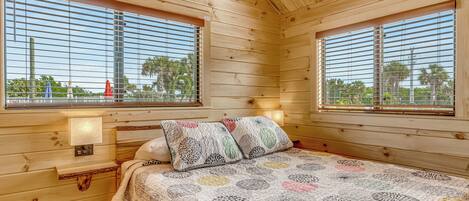 A wooden cabin bedroom with a bed, two windows, and a nightstand.