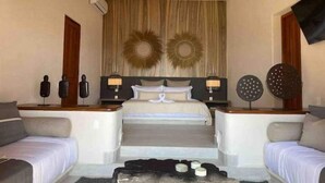 Habitación de hotel con cama, dos mesitas de noche, sofá, mesa de centro y televisor.
