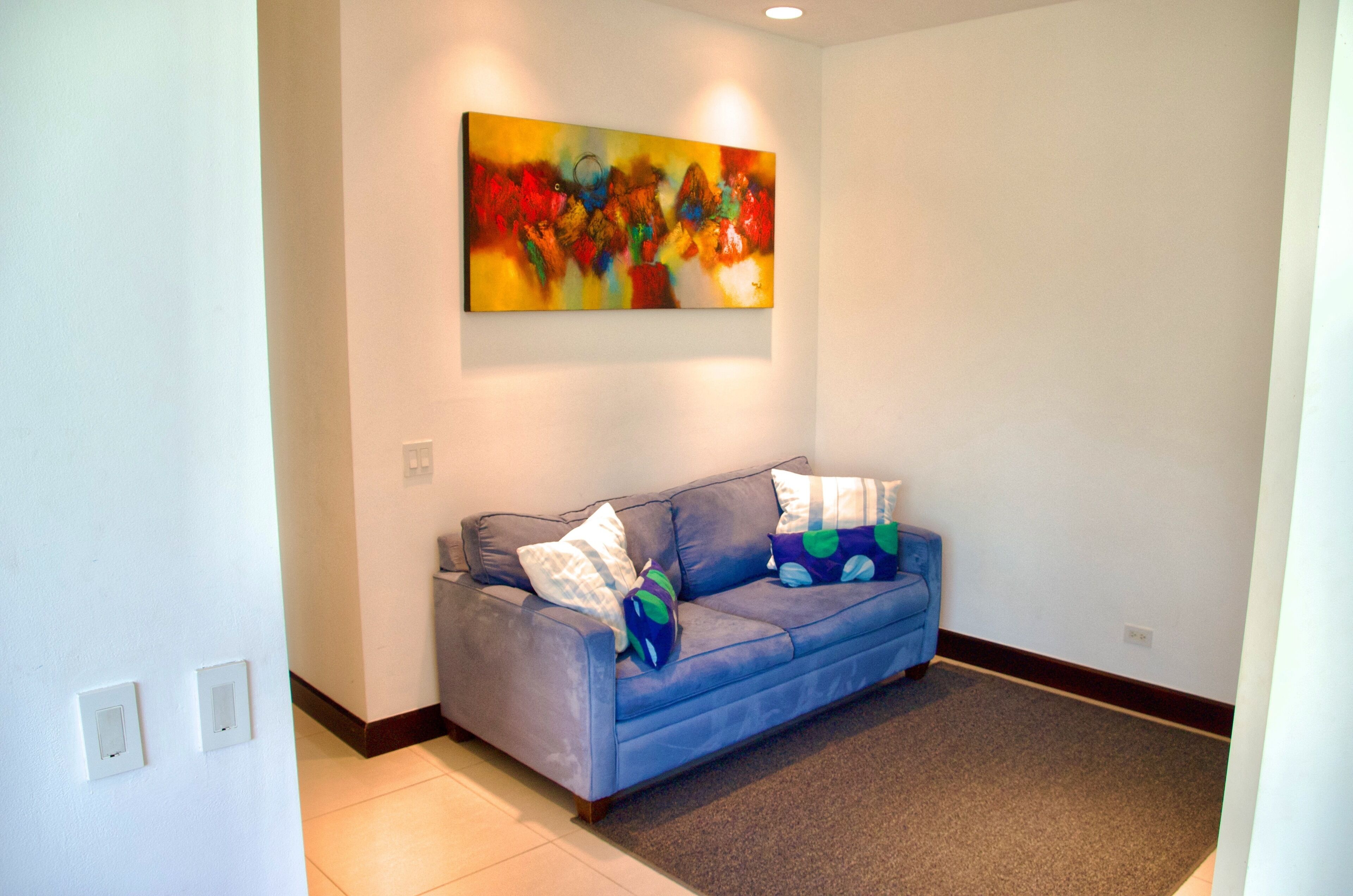 Una stanza con un divano blu, un quadro astratto dai colori vivaci appeso al muro e un pavimento tappezzato.