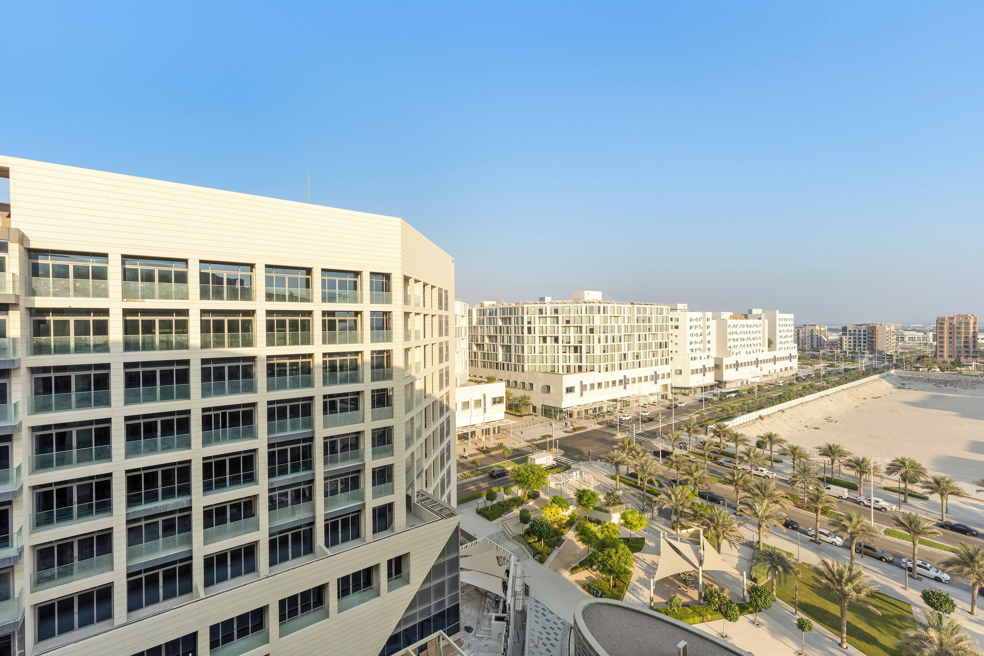 A modern hotel with multiple floors, a beach view, and a parking area with palm trees.