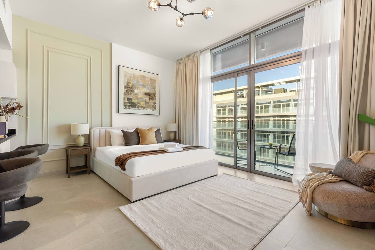 Een moderne hotelkamer met een groot bed, een zithoek met een bank en fauteuils, een eettafel en een balkon met uitzicht op de stad.