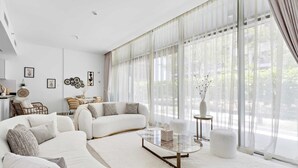 A modern living room with a white sofa, a glass coffee table, and a large window with sheer curtains. - Silkhaus Park View Tower - Saadiyat Island (Abu Dhabi)
