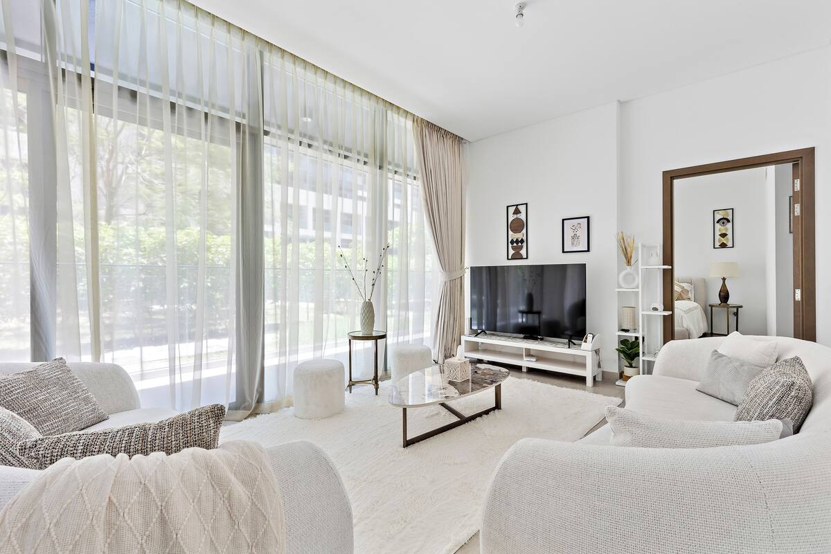 Een moderne woonkamer met een grote televisie, witte meubels en uitzicht op groen.