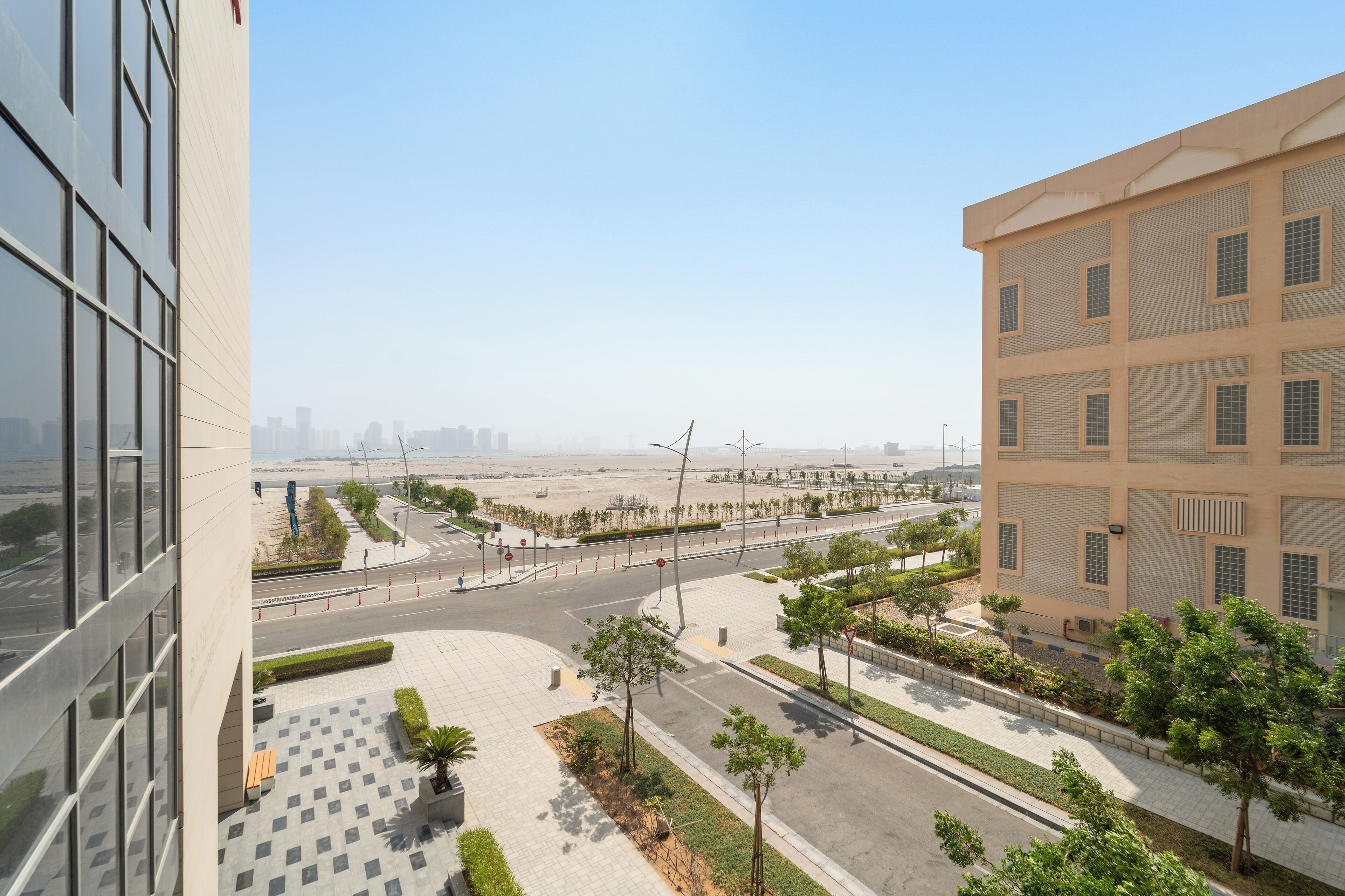 A modern building with a glass facade and a spacious courtyard with trees and a paved walkway.