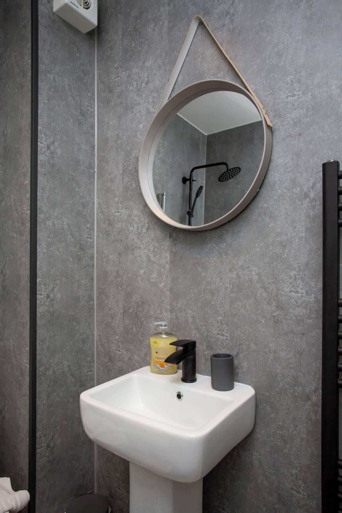 Une salle de bain avec un lavabo blanc, un miroir rond et une pomme de douche.