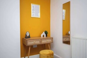 A room with a wooden desk, a mirror, a framed note, and a small stool.