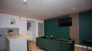 Una cocina moderna con barra, televisión de pantalla plana y una pared de acento verde.