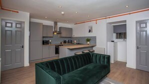 Una cocina moderna con gabinetes grises, una isla central y un sofá verde en la sala.