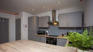 Una cocina moderna con gabinetes grises, una campana extractora de acero inoxidable, una encimera de madera y una planta en maceta.