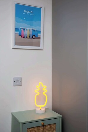 A framed picture of a van with surfboards, a neon pineapple light, and a switch on the wall. - Bondi beach Getaway - One bedroom apartment (Tyne and Wear)