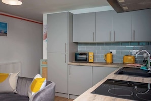 A modern kitchen with grey cabinets, a microwave, a kettle, and a sink.