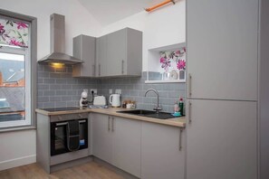 Eine kompakte Küche mit grauen Schränken, einem Backofen, einer Spüle und einem Fenster mit floralem Dekor.