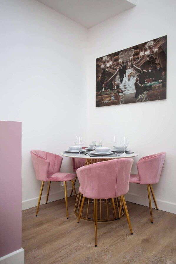 A dining area with a round table, pink chairs, and a framed picture on the wall.