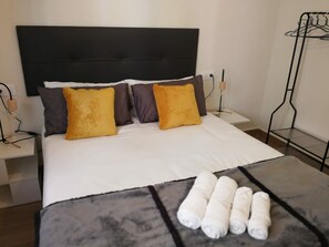 A neatly made bed with a black headboard, two pillows with a yellow accent, and a gray blanket with rolled towels on the bed.