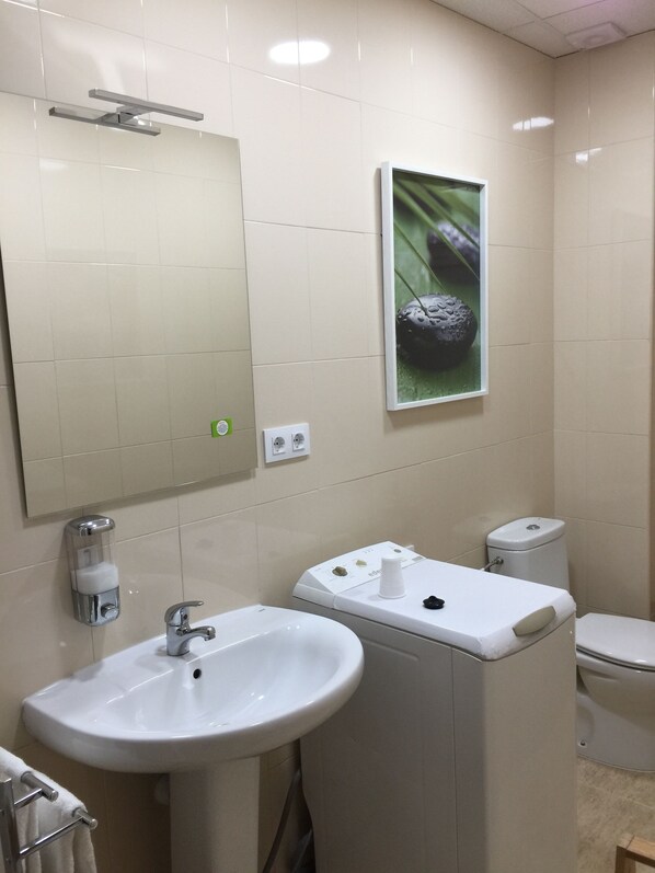 A bathroom with a white sink, mirror, and toilet. There is a green plant on the wall and a white towel rack.